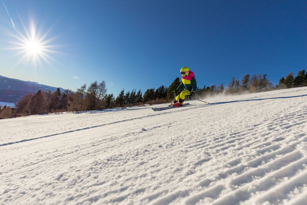 Ein Skifahrer im Skigebiet Fanningberg im Lungau, von der Seite fotografiert, während er die Piste hinunterfährt. Danach geht es auf in die Hüte, der Gaudi und dem Après-Ski steht nichts mehr im Weg.