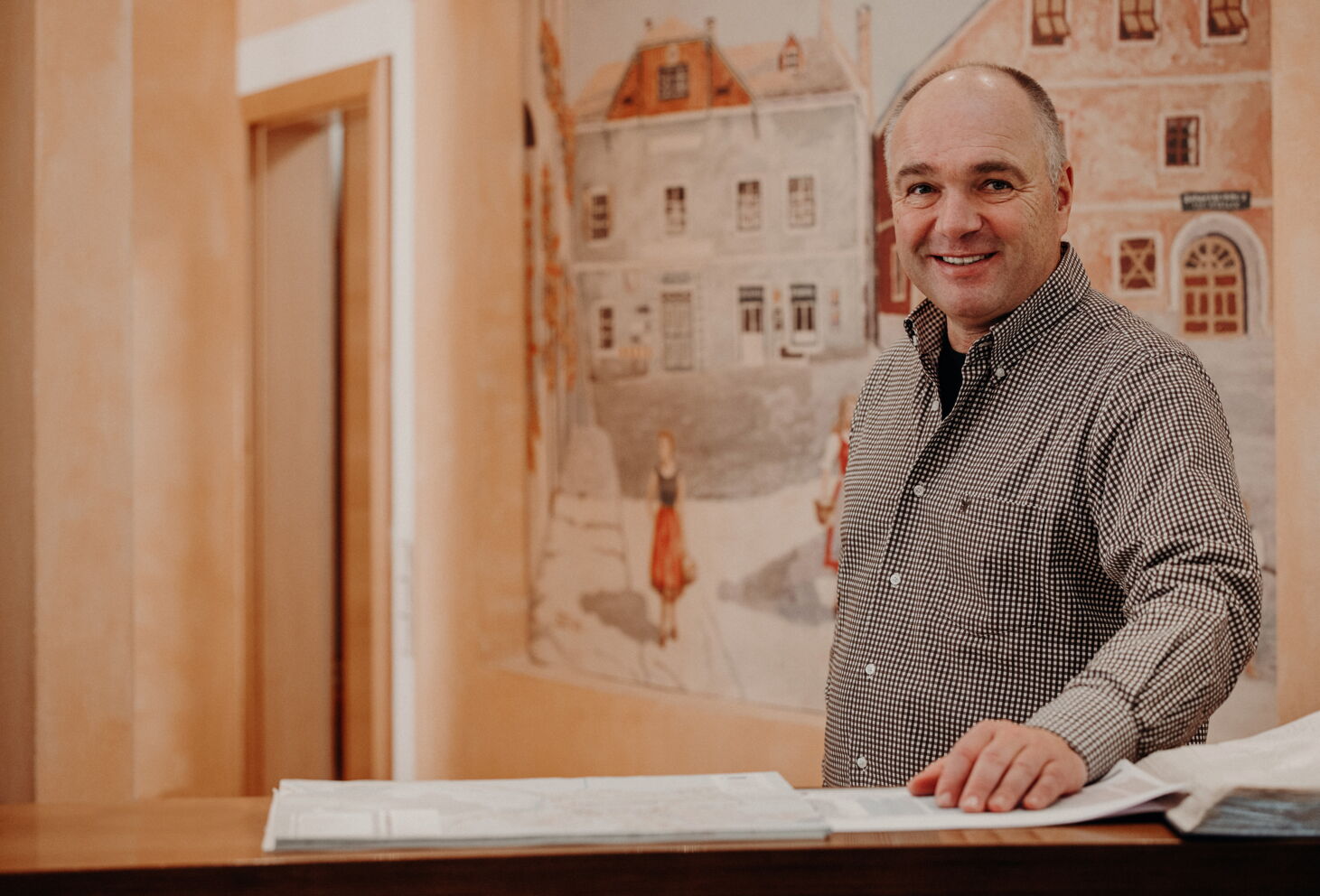 Lächelnder Mann an einem Empfangstresen mit Wandbild im Hintergrund.