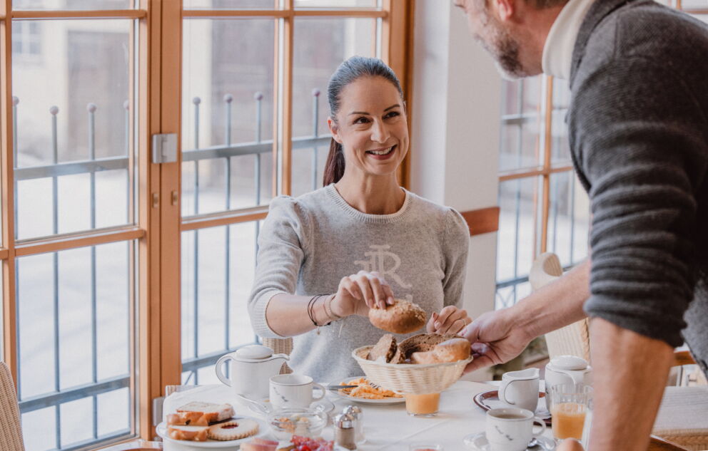 Woman enjoys breakfast with bread rolls and drinks in a cozy atmosphere.