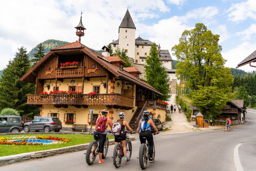 Radfahrer vor traditionellem Haus und Schloss in malerischer Berglandschaft