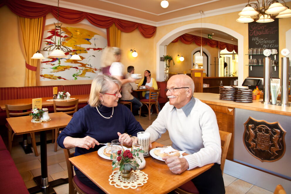 Älteres Paar genießt Kuchen in gemütlichem Café mit freundlicher Bedienung.