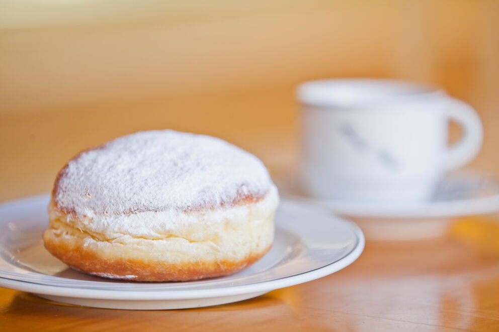 Berliner with powdered sugar on a plate, a cup of coffee next to it.