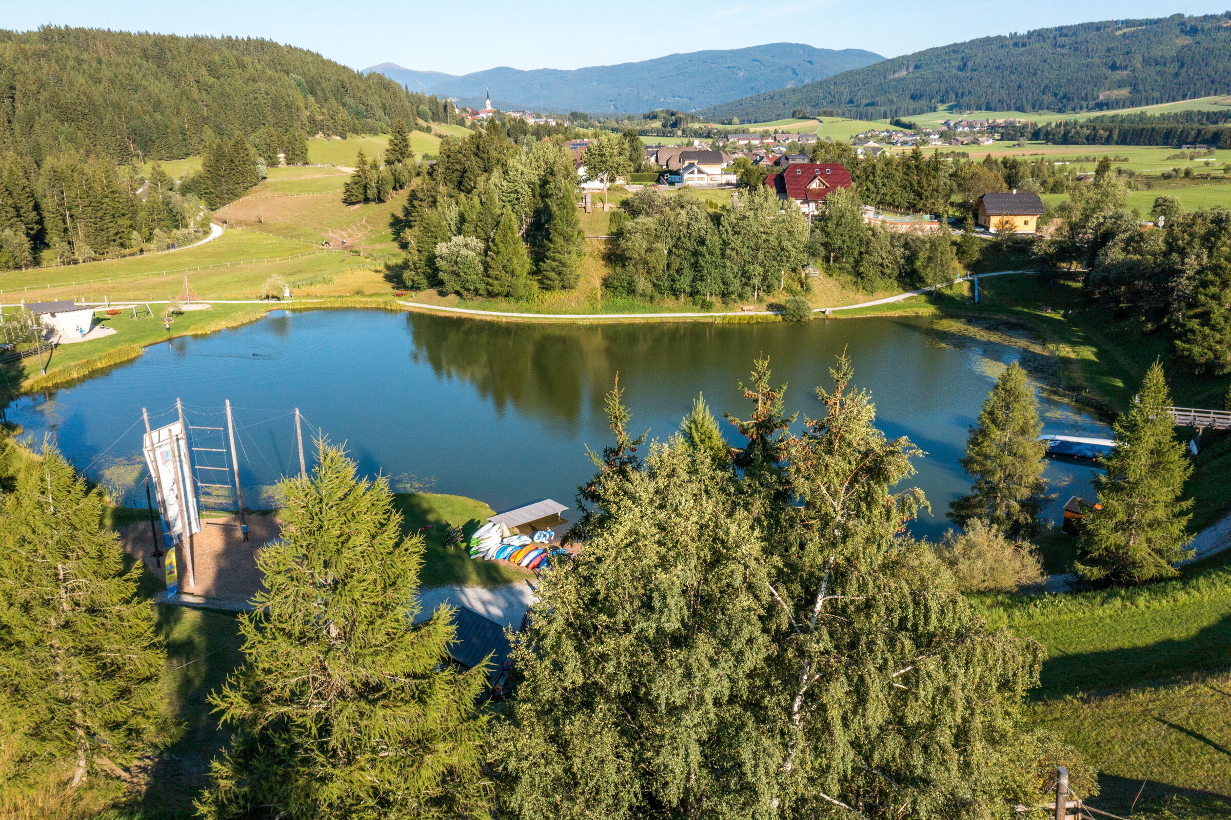 Malerischer Bergsee mit umliegenden Wäldern und charmanten Häusern bei Sonnenlicht.