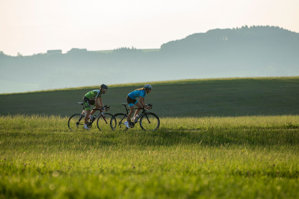 Zwei Radfahrer in grüner Landschaft unter strahlendem Himmel.