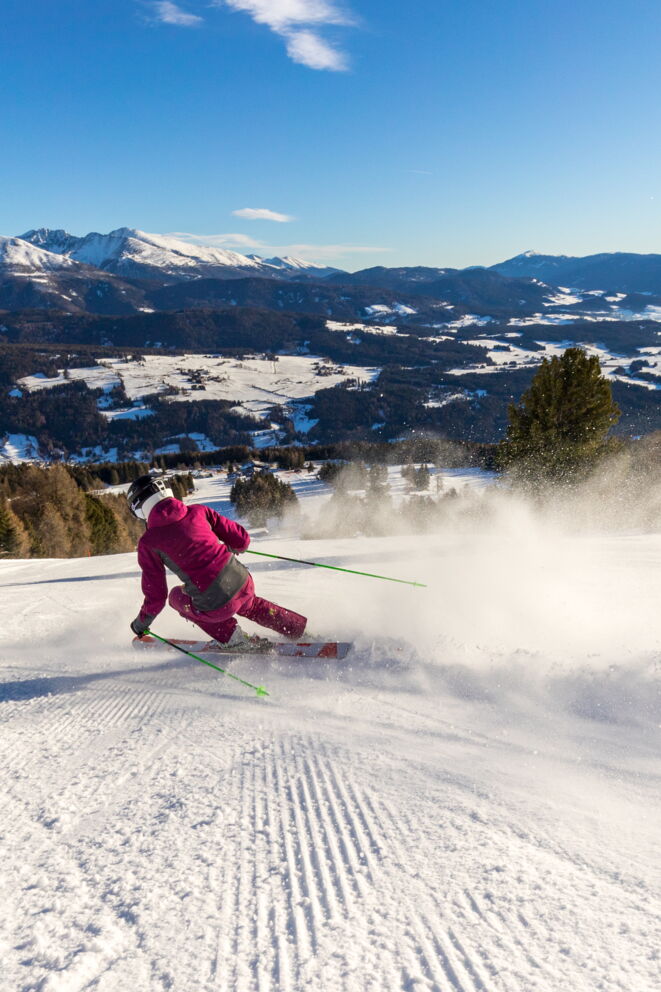 Skifahrer in roter Kleidung gleitet elegant über verschneite Piste mit Bergpanorama.