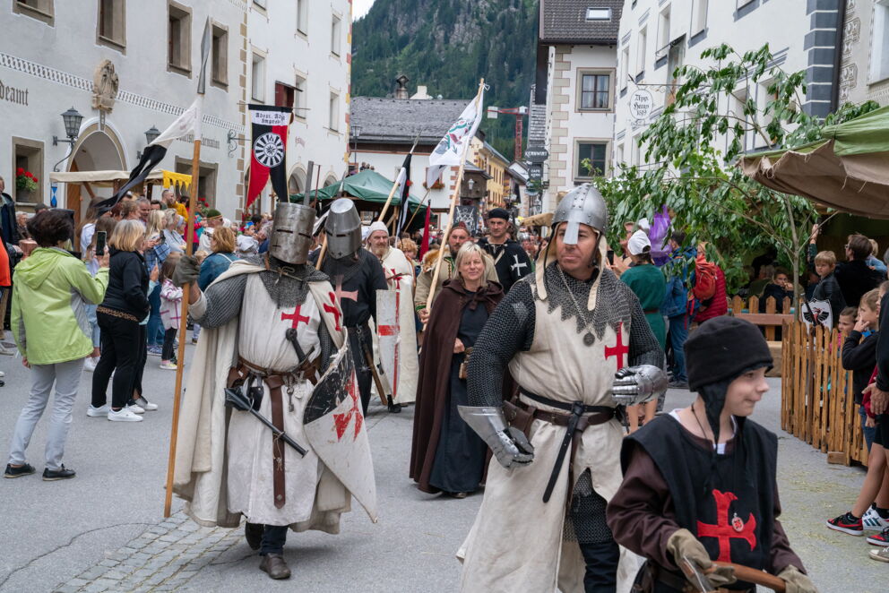 Menschen in mittelalterlichen Kostümen auf einem belebten Straßenfest mit historischer Kulisse.