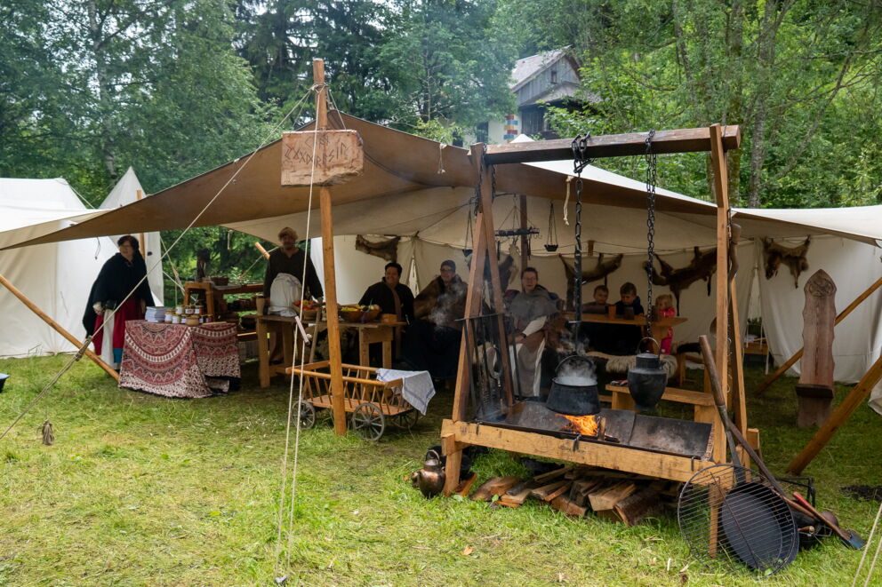 Zeltlager mit Menschen in mittelalterlicher Kleidung und Kochstelle im Freien