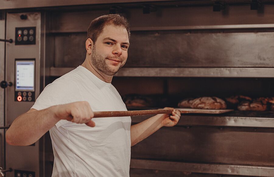 Bäcker zieht frisches Brot aus dem Ofen mit handwerklicher Präzision.