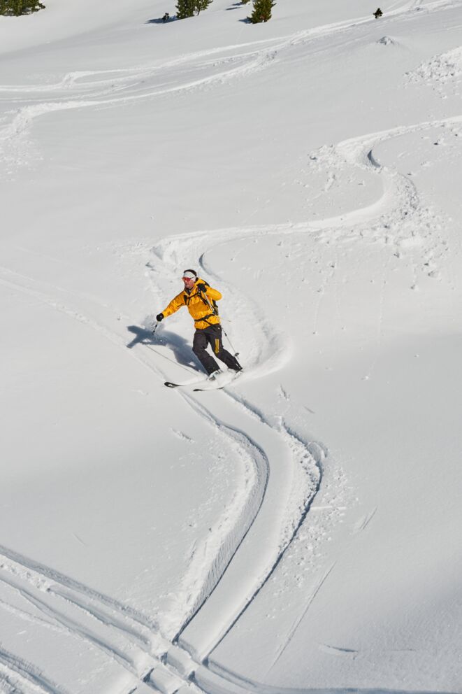Skifahrer zieht Schwünge im frischen Pulverschnee bei strahlendem Sonnenschein.