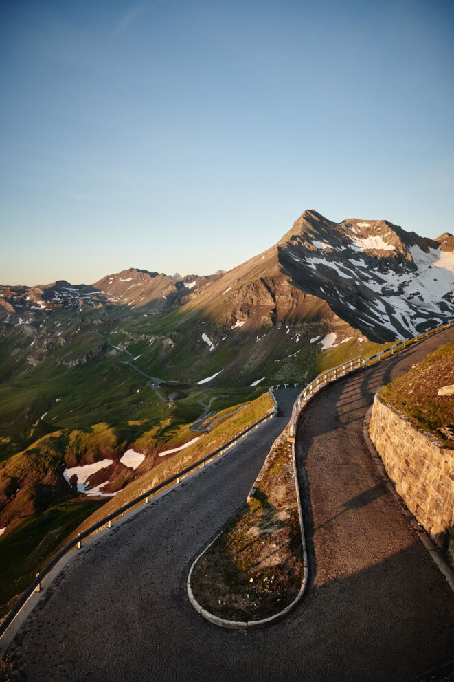 Windige Straße führt durch majestätische Berglandschaft unter klarem Himmel.