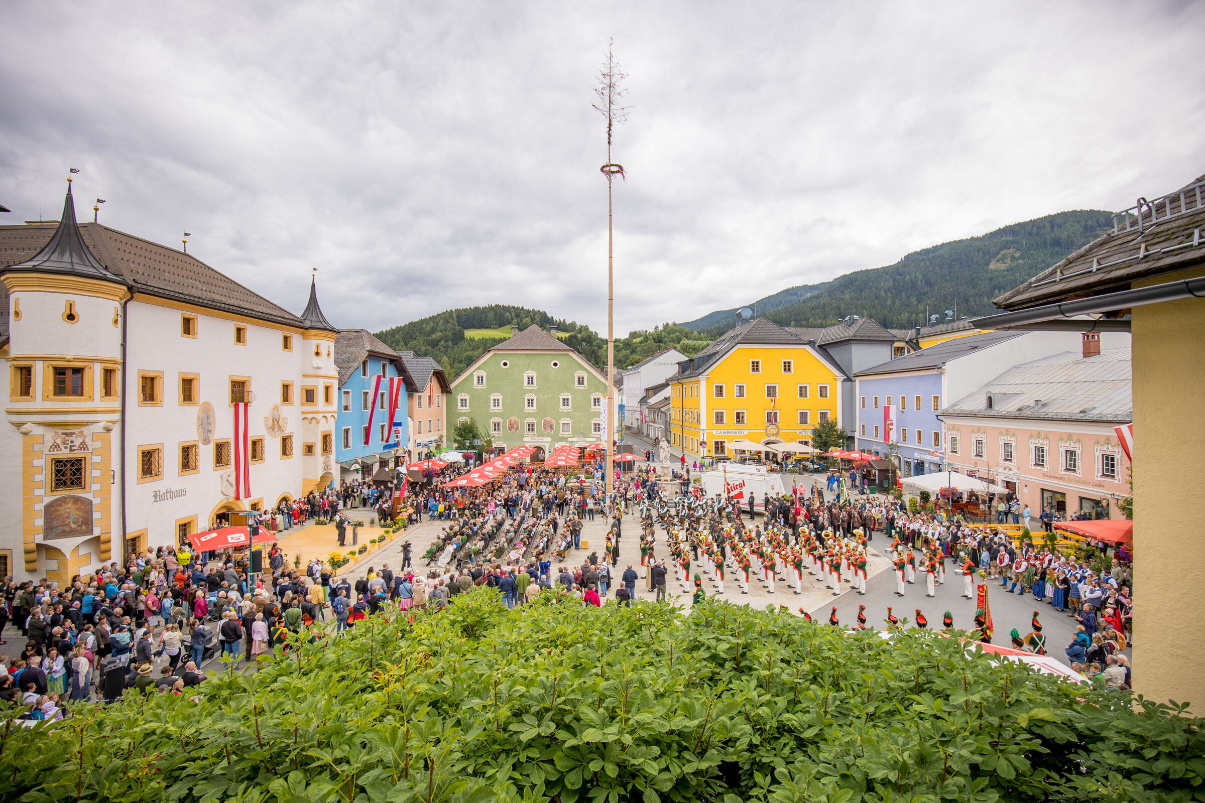Buntes Stadtfest mit Menschenmenge und traditionellen Trachten in idyllischer Bergkulisse.