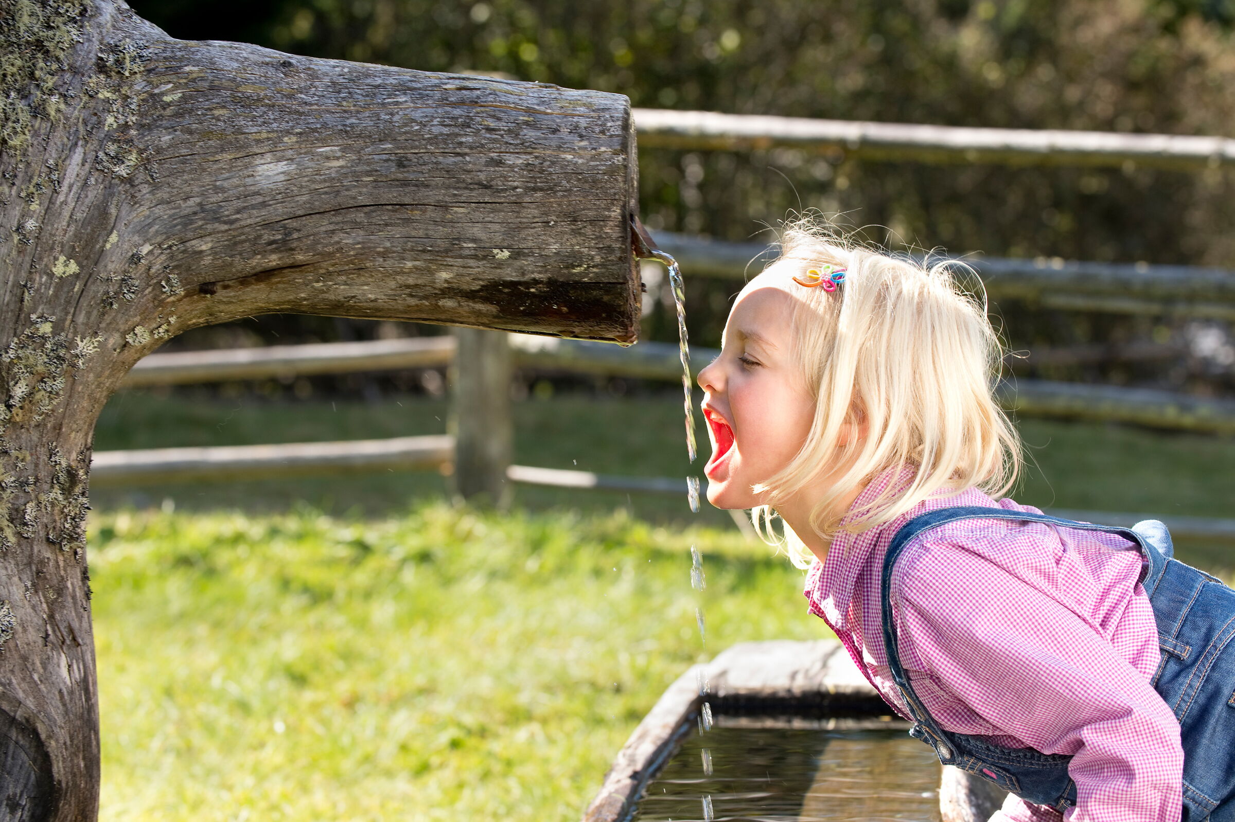 Kind trinkt aus einem natürlichen Holzbrunnen im Freien