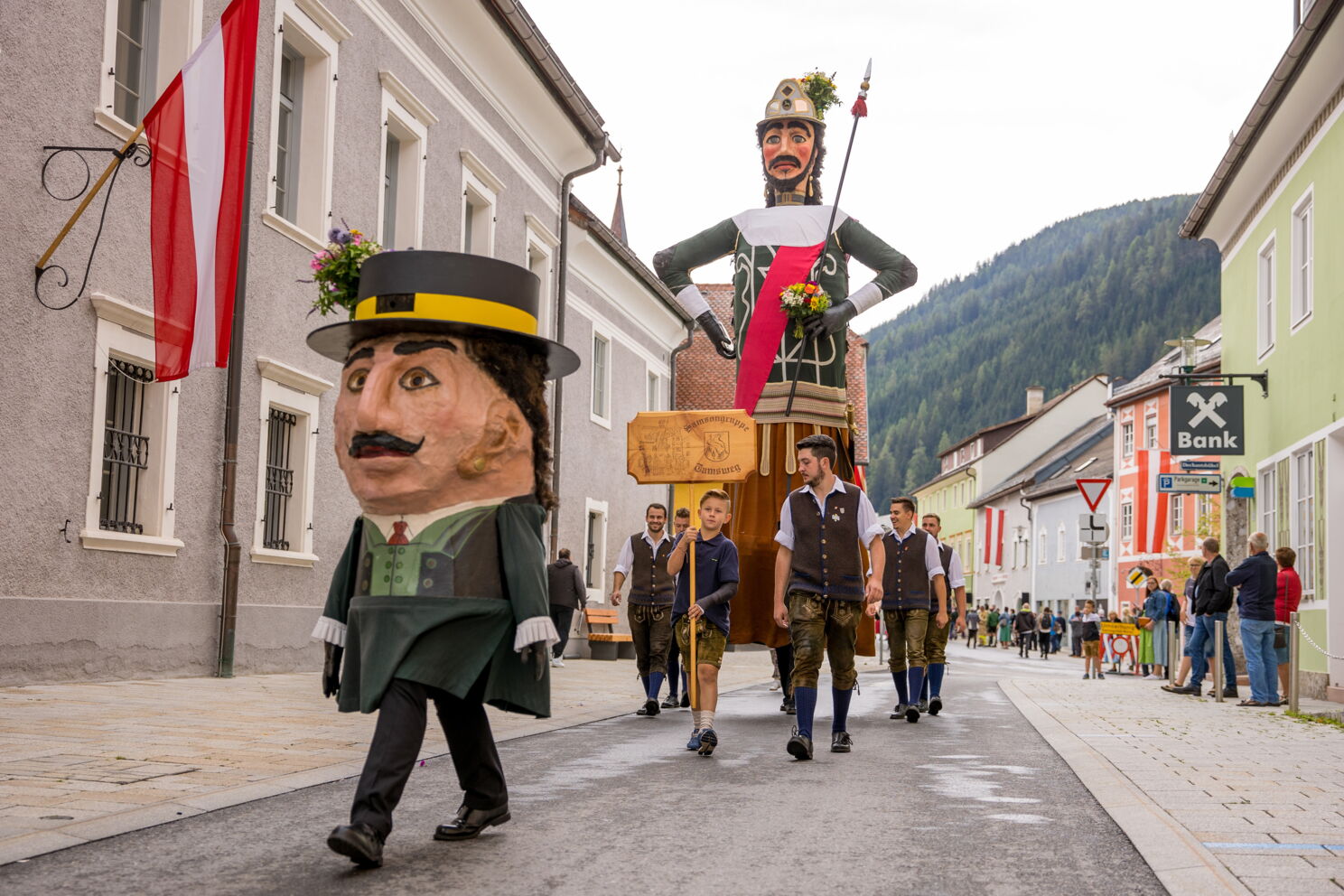 Menschen in Trachten führen große Figuren in einem farbenfrohen Straßenumzug an.