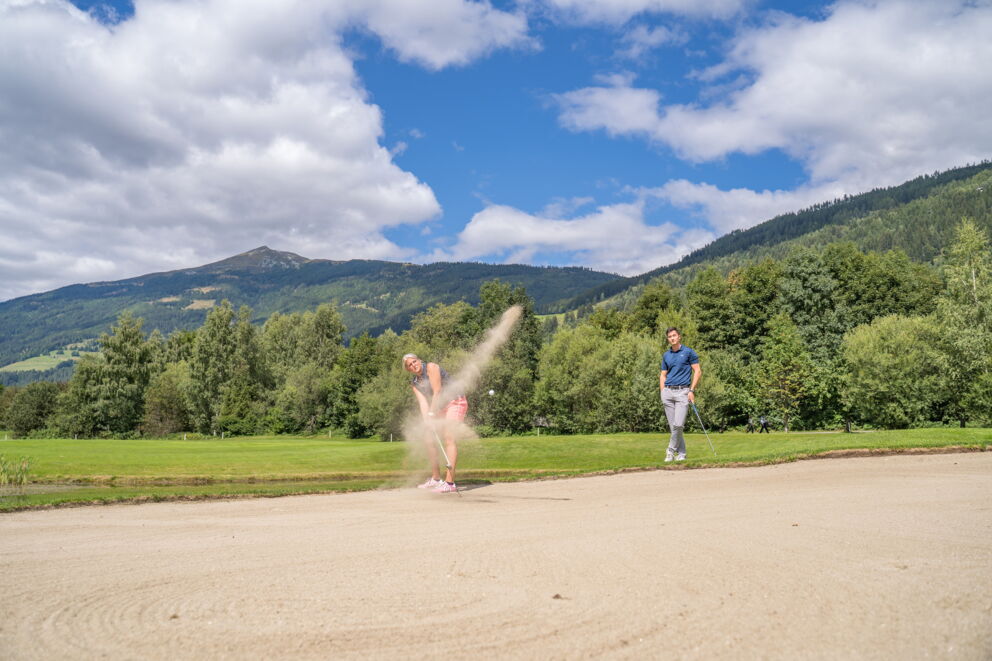 Golfer und Begleiter auf grünem Rasen mit majestätischen Bergen im Hintergrund.