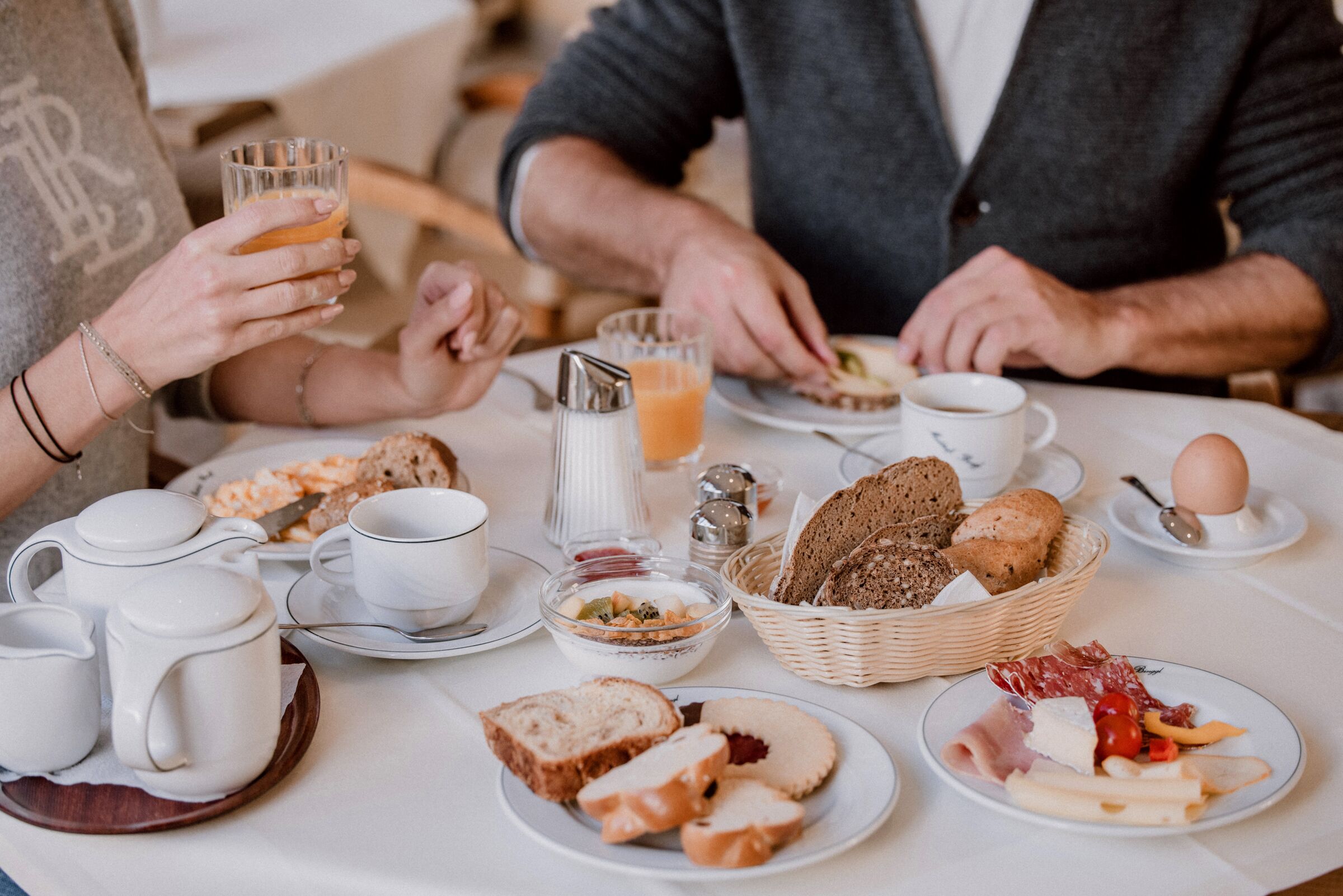 Frühstückstisch mit Brot, Gebäck, Aufschnitt, Orangensaft und heißem Tee.