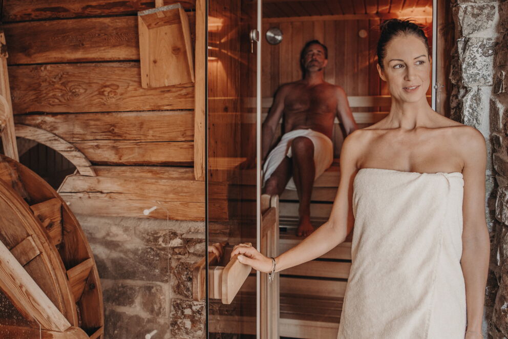 Zwei Personen in Sauna mit Holzwänden, entspannte Atmosphäre, Handtücher.