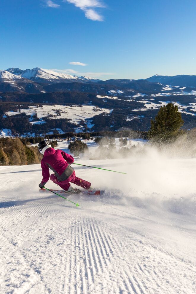 Skifahrer in roter Kleidung gleitet elegant über verschneite Piste mit Bergpanorama.