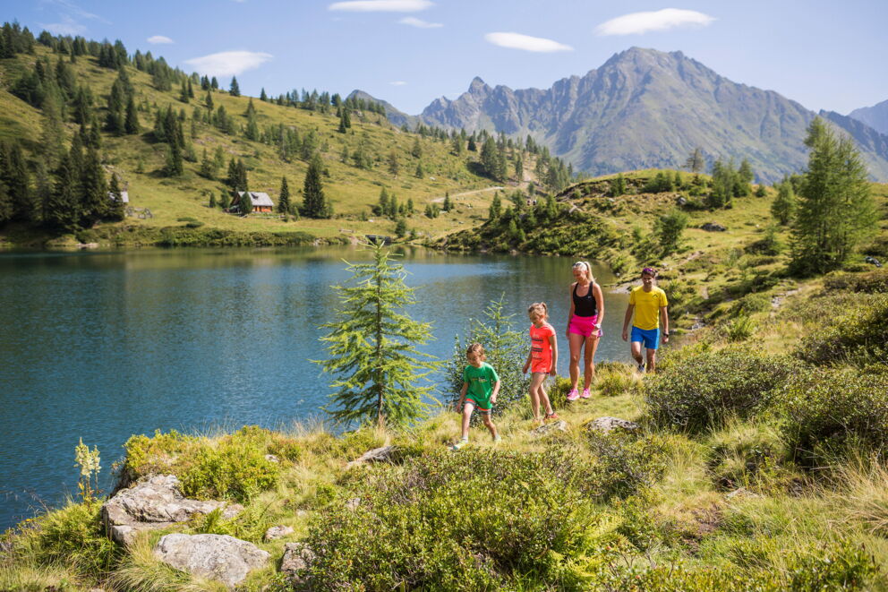 Familie wandert an einem klaren Bergsee mit malerischer Alpenlandschaft.