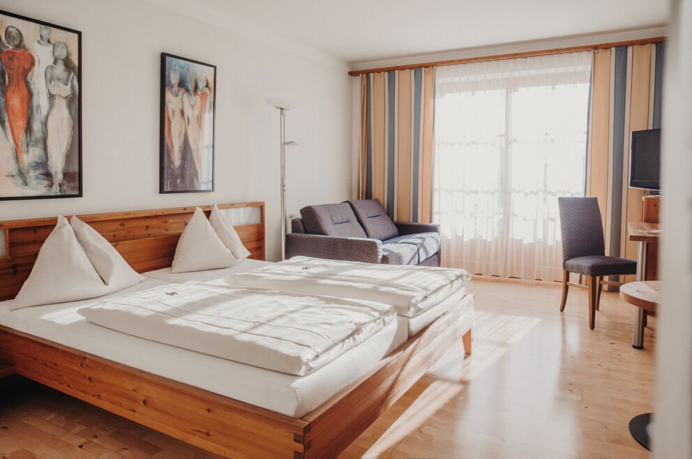 Helles Schlafzimmer mit Holzmöbeln, Sofa und Kunstbildern an den Wänden.
