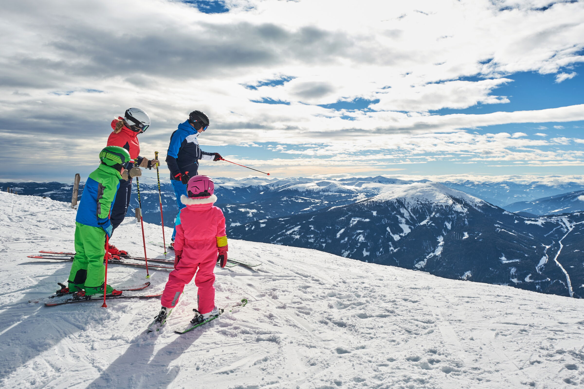 Familie auf verschneitem Berg mit weiten Blicken über die Alpenlandschaft.