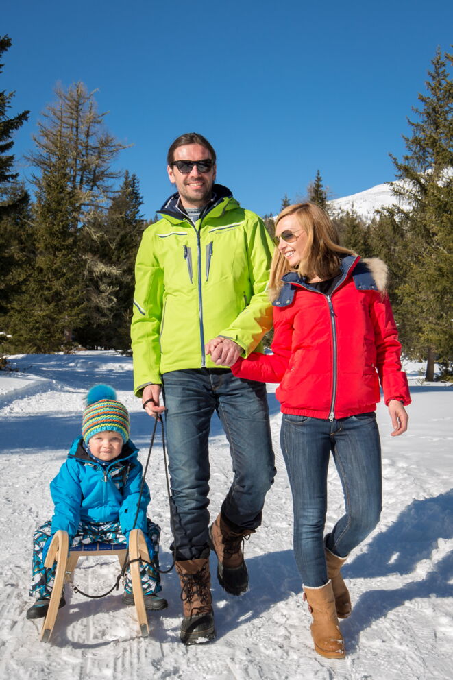 Familie mit Schlitten genießt sonnigen Wintertag im Schnee.