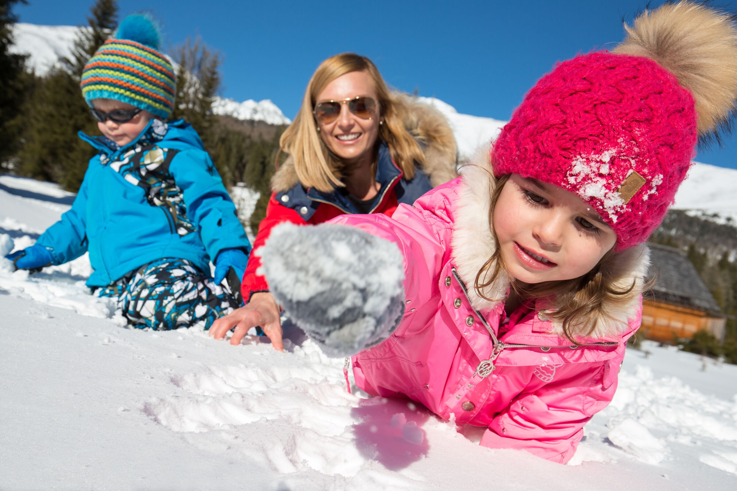 Familie genießt fröhliche Wintermomente im glitzernden Schnee vor malerischer Bergkulisse.