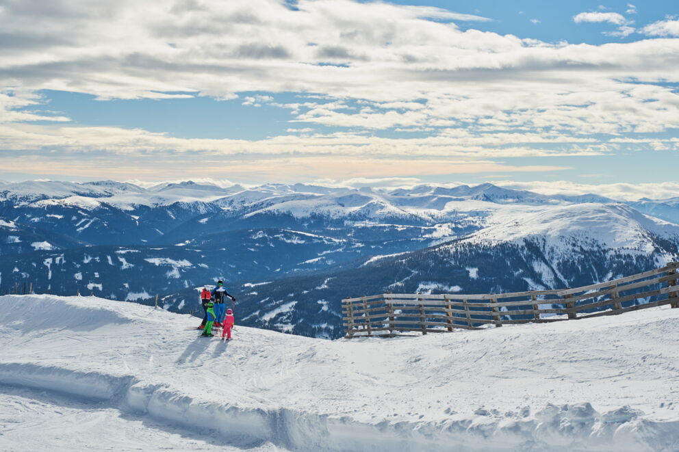 Familie genießt Skifahren auf schneebedecktem Berg mit weitem Blick auf die Alpen.