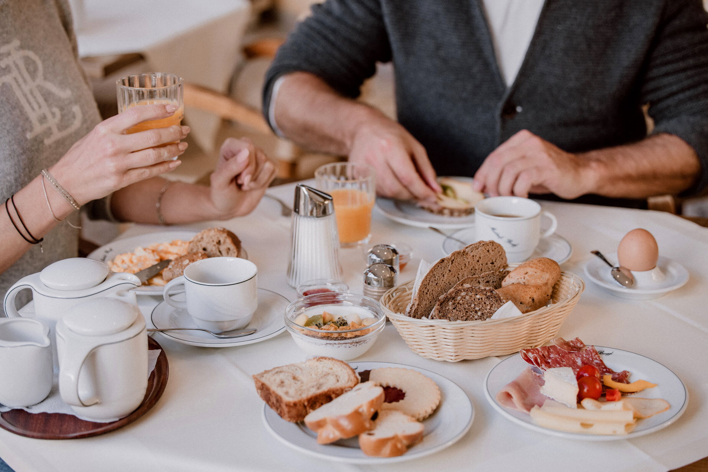 Frühstückstisch mit Brot, Gebäck, Aufschnitt, Orangensaft und heißem Tee.