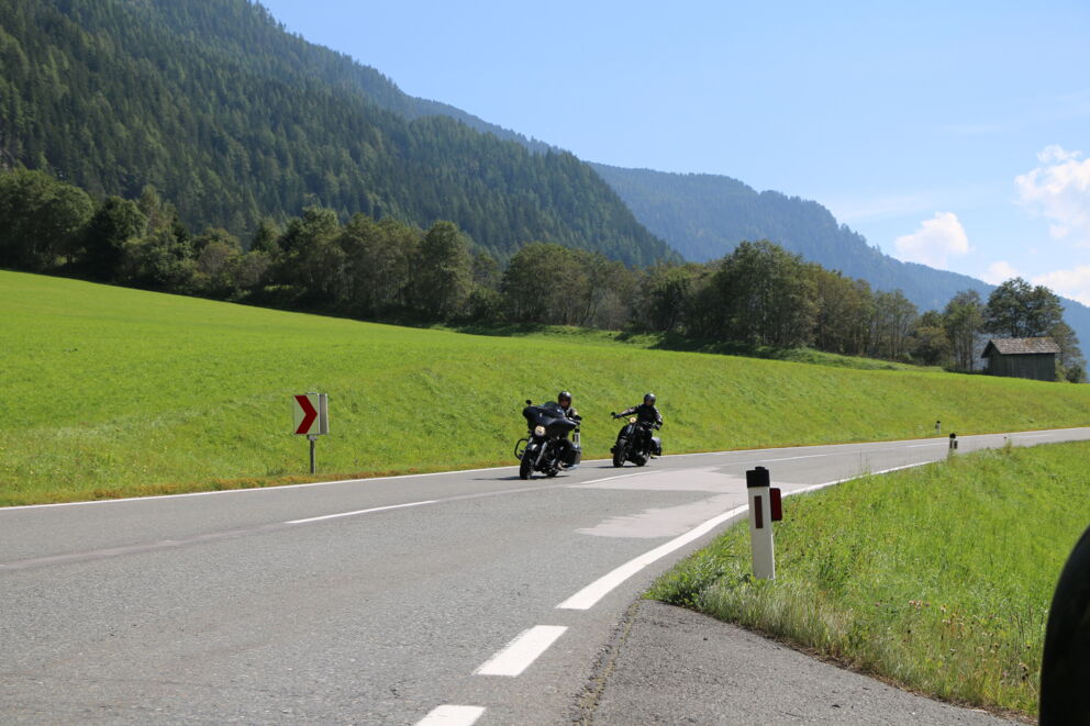Zwei Motorradfahrer auf einer Bergstraße in Österreich in einer leichten Rechtskurve.