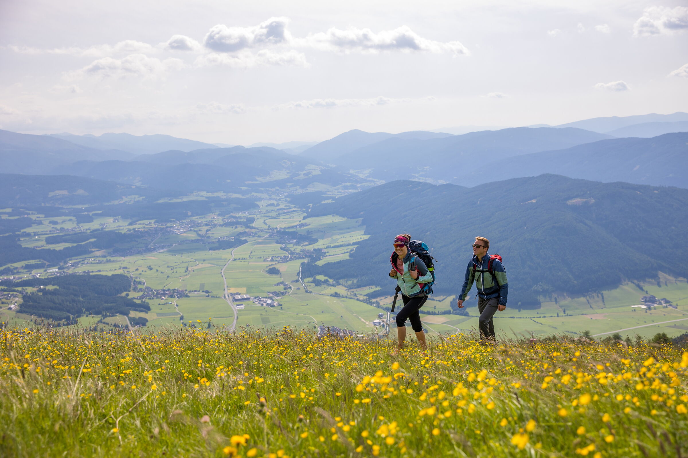 Zwei Wanderer genießen eine malerische Berglandschaft voller Blumen und Weitblick.