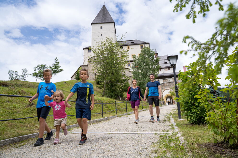 Familie spaziert glücklich bei sonnigem Wetter vor einer historischen Burg.