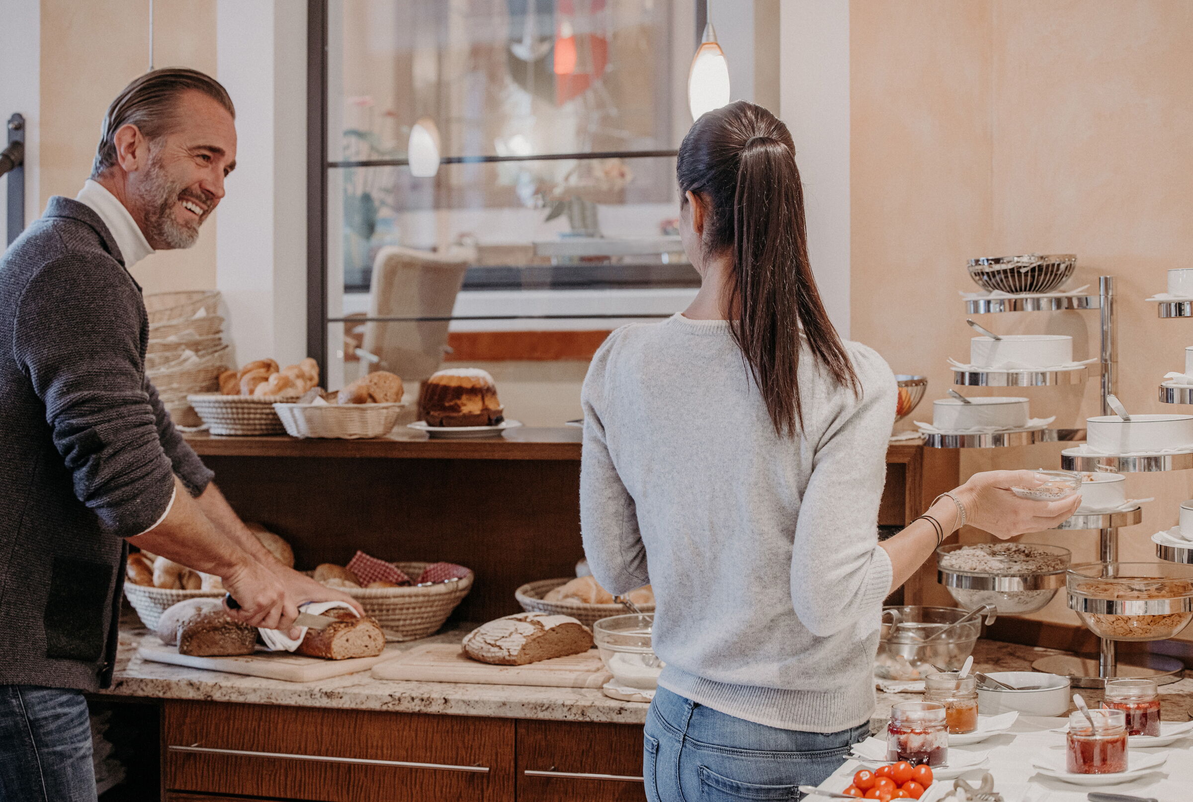 Man and woman enjoy a rich breakfast buffet with fresh bread and jam.