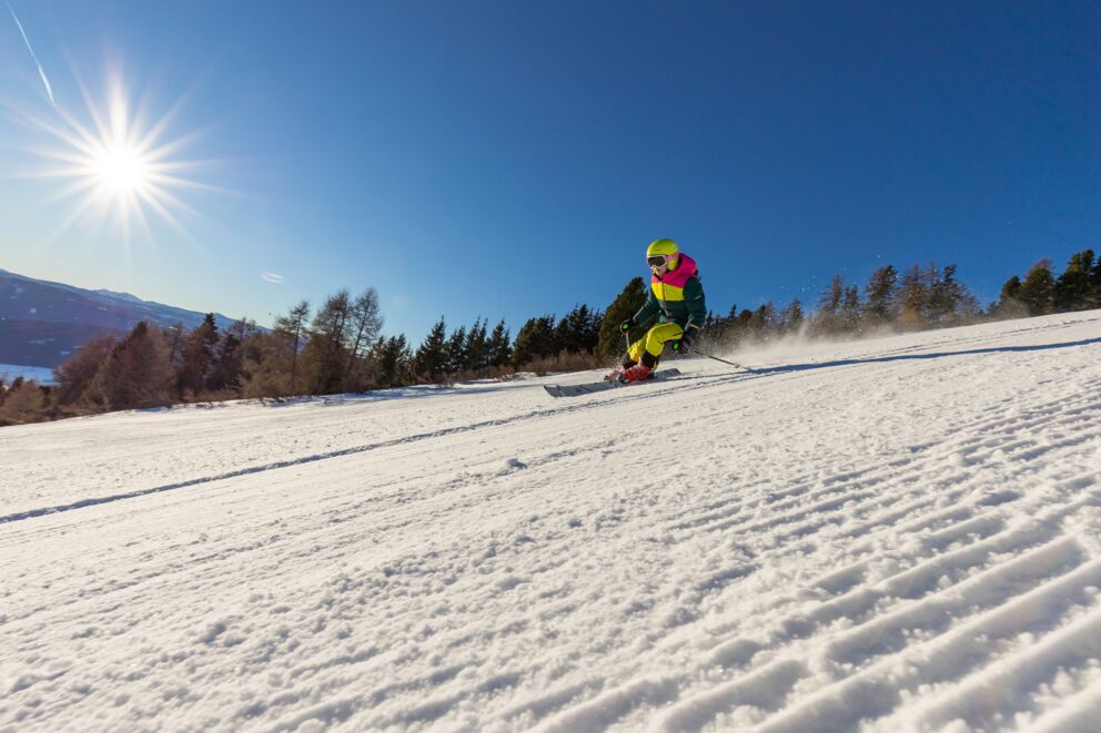 Skifahrer gleitet schwungvoll die Piste hinunter bei klarem Sonnenschein und blauem Himmel.