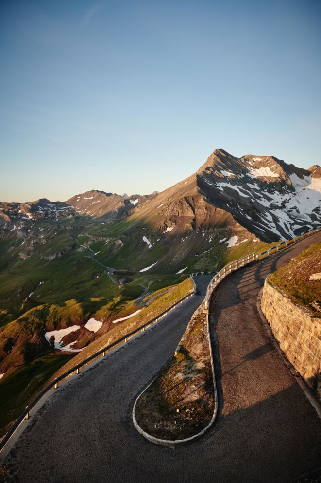 Windige Straße führt durch majestätische Berglandschaft unter klarem Himmel.
