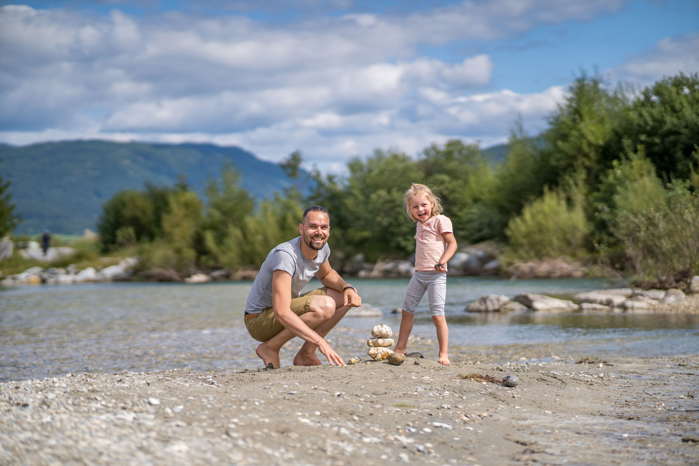 Vater und Tochter genießen einen sonnigen Tag am Flussufer mit Steinhaufen.