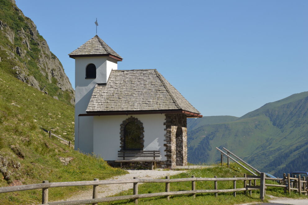 Kleine Kapelle inmitten alpiner Berglandschaft bei strahlend blauem Himmel.