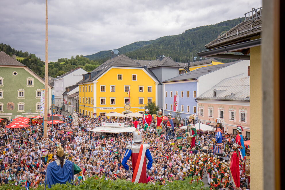 Buntes Fest mit farbenfrohen Kostümen und einer großen Menschenmenge unter wolkigem Himmel