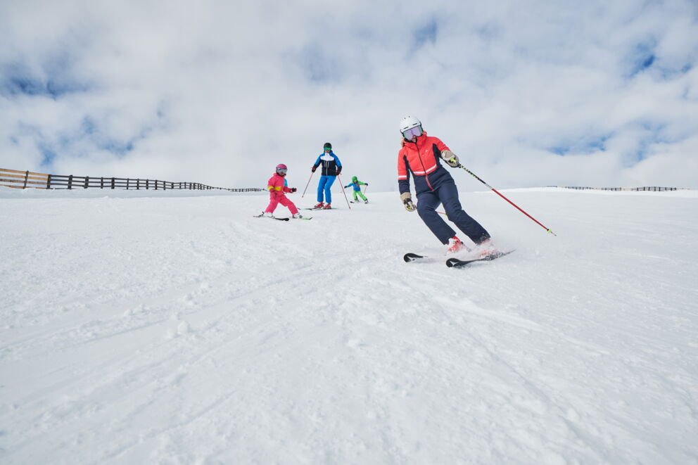 Familiengruppe genießt Skifahren auf schneebedecktem Hang unter blauem Himmel.