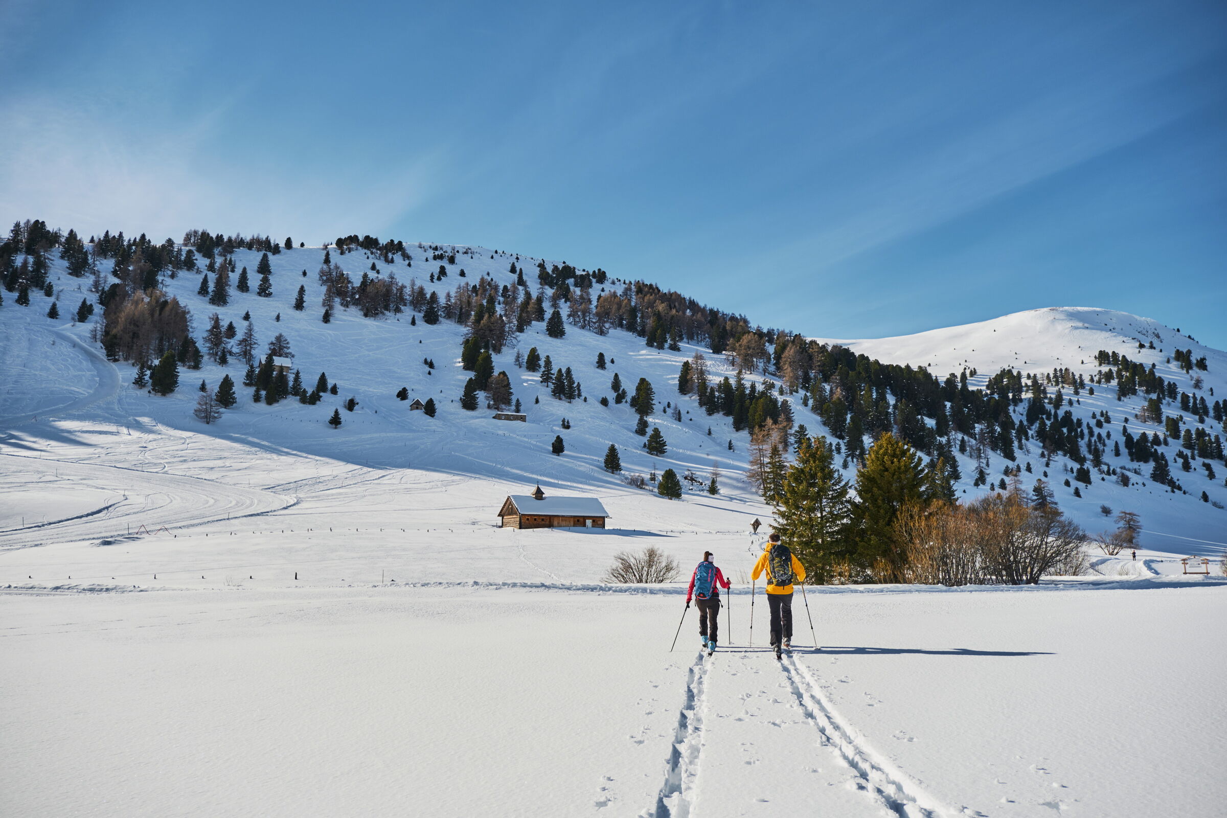 Zwei Skitourengeher in verschneiter Berglandschaft unter klarem, blauem Himmel.