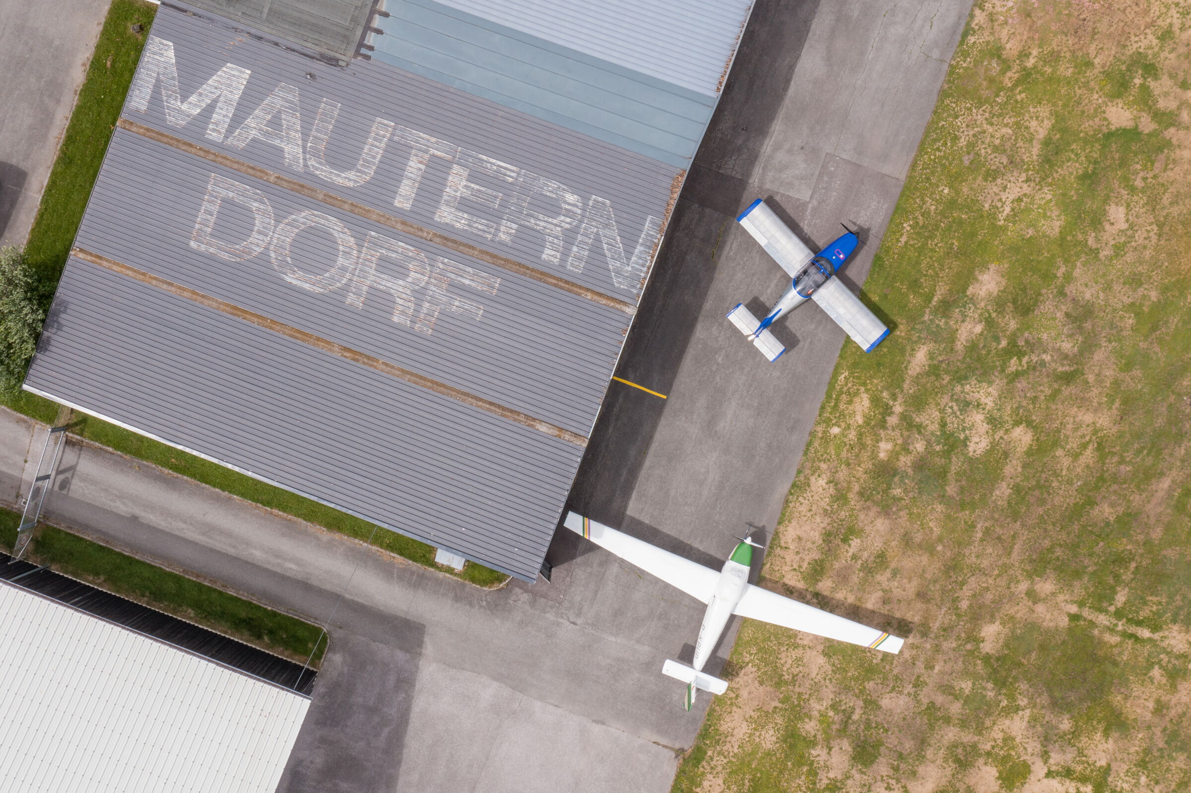 Luftaufnahme eines Hangars mit zwei kleinen Flugzeugen auf einer Grasfläche.