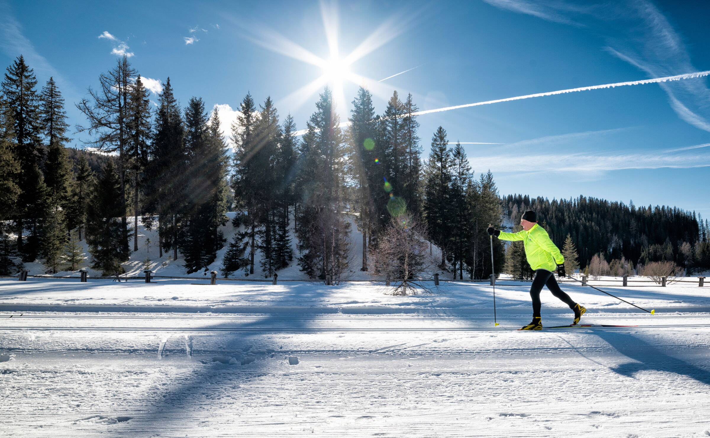 Langläufer in leuchtender Jacke unter strahlendem Sonnenschein auf schneebedeckter Loipe.