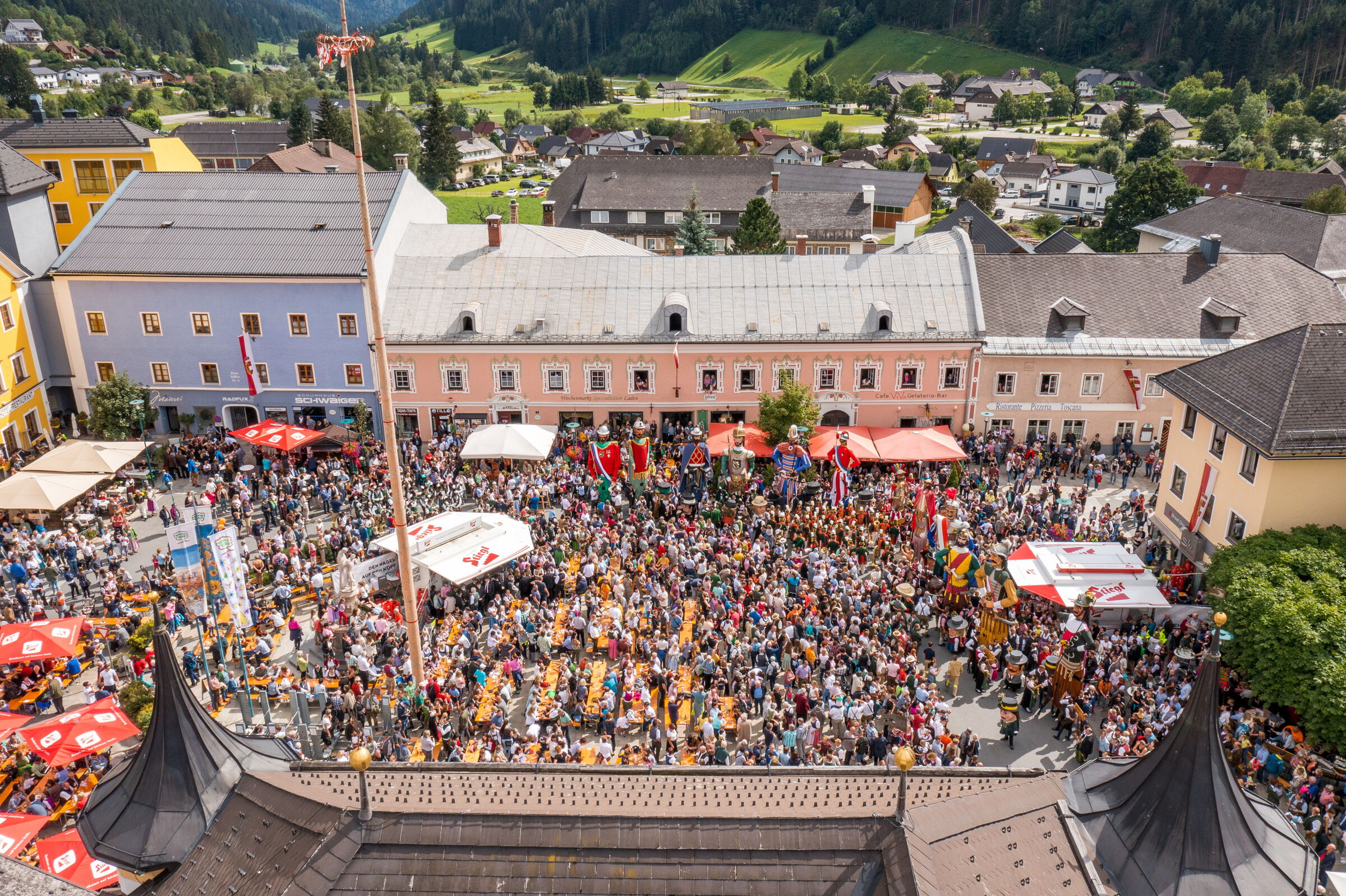 Buntes Straßenfest mit Menschenmenge, traditionellen Trachten und farbenfrohen Häusern im Hintergrund.