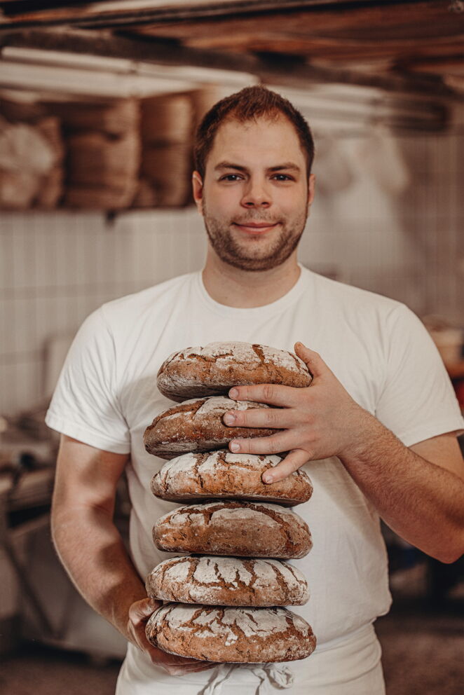 Der Bäcker Florian Binggl hält sechs frisch in der hauseigenen Bäckerei in Mauterndorf gebackene Brote in den Händen.