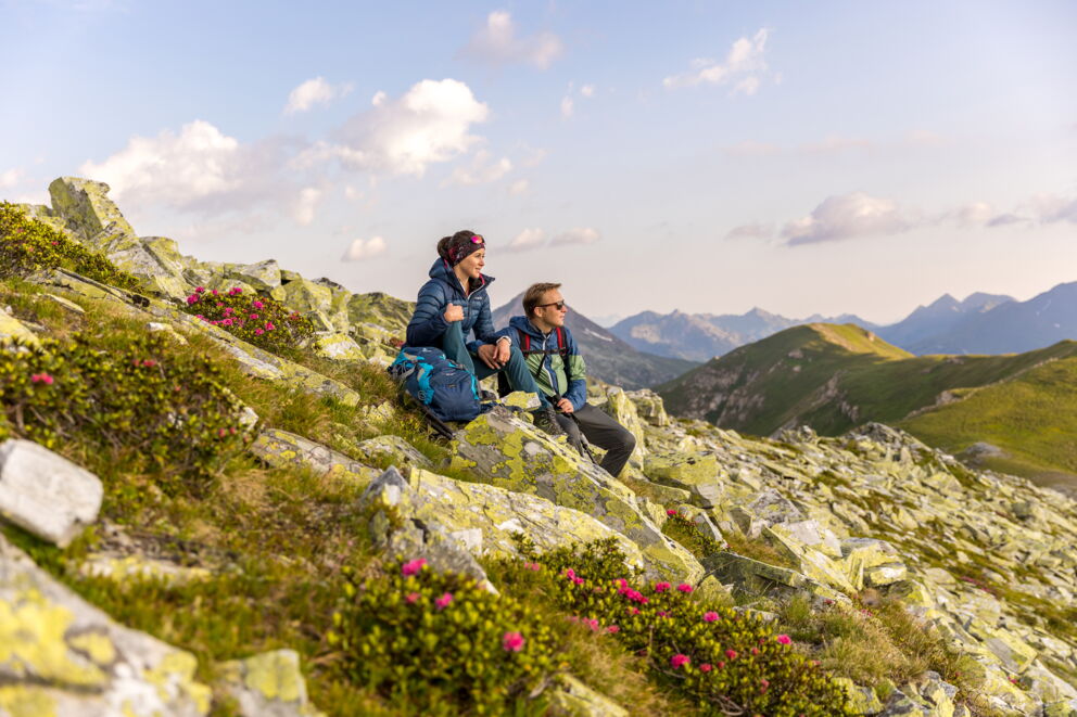 Zwei Wanderer genießen den Ausblick auf die malerische Berglandschaft bei Sonnenuntergang.