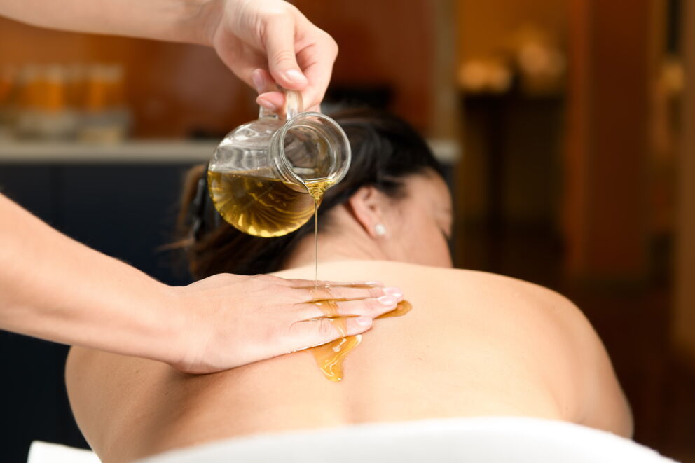 Hände gießen Öl auf Rücken für entspannende Massage in wohliger Spa-Atmosphäre.