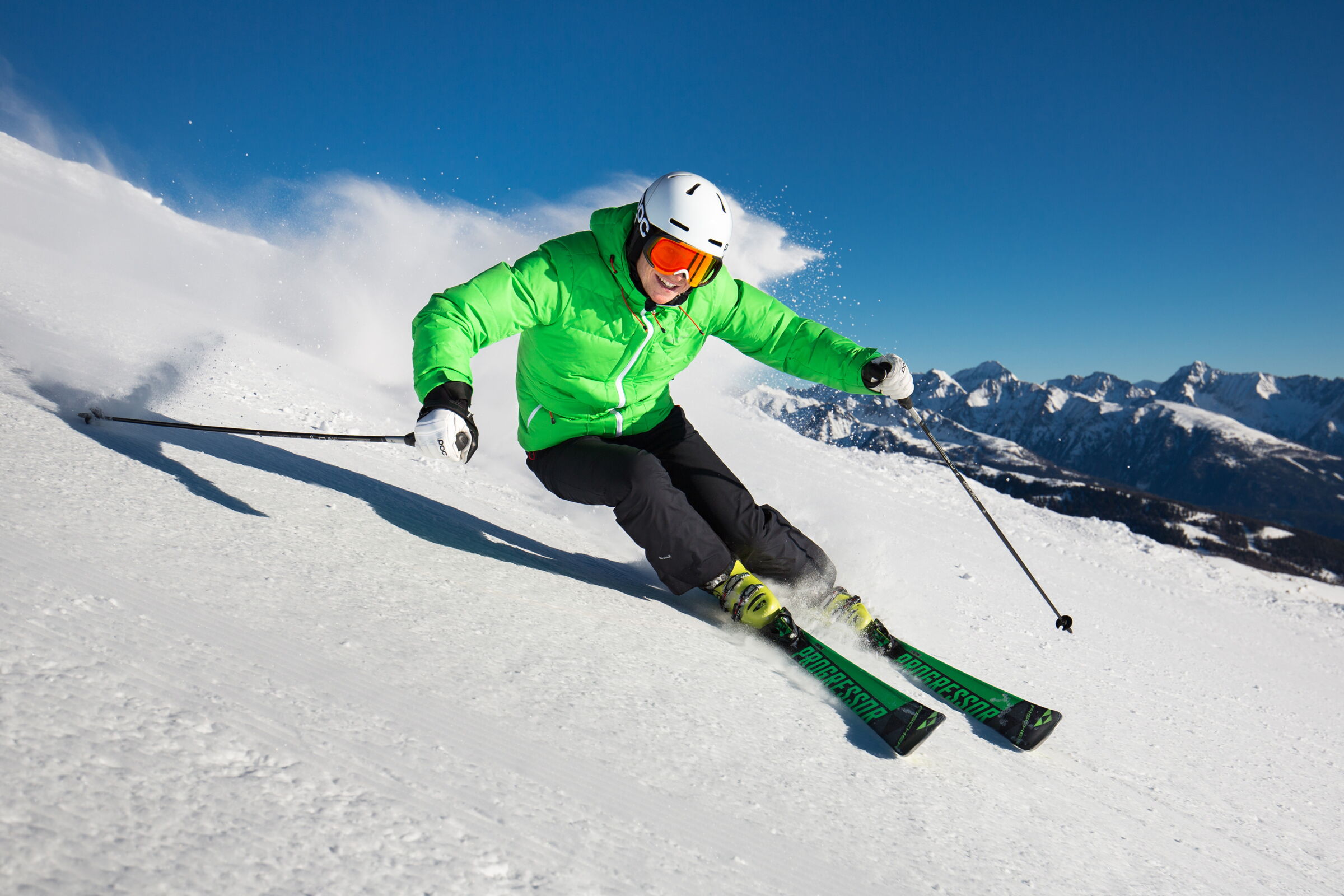 Skifahrer in grüner Jacke auf verschneiter Piste vor beeindruckendem Bergpanorama.