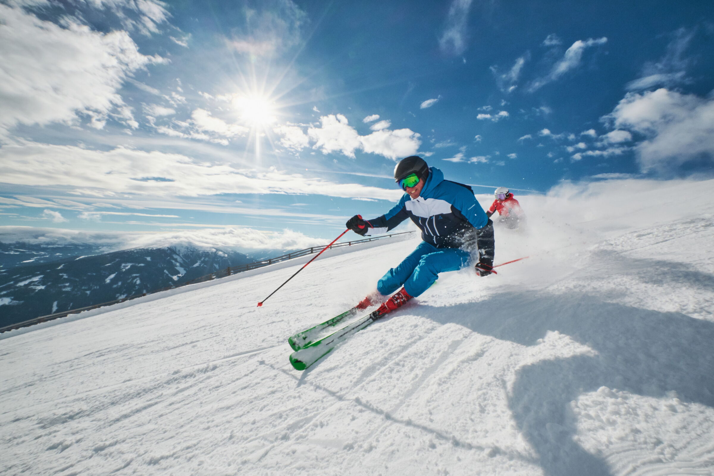 Zwei Skifahrer auf einer schneebedeckten Piste bei strahlendem Sonnenschein.