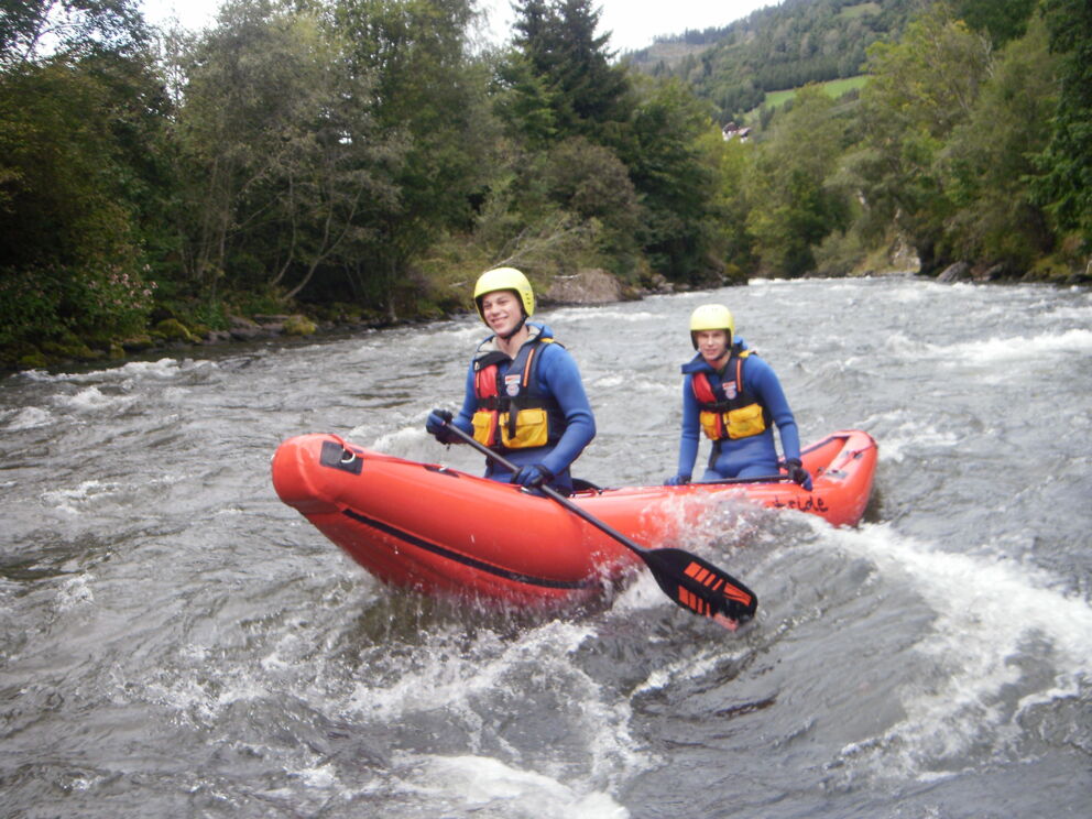 Zwei Personen im Kanu auf einem sprudelnden Fluss inmitten grüner Natur.