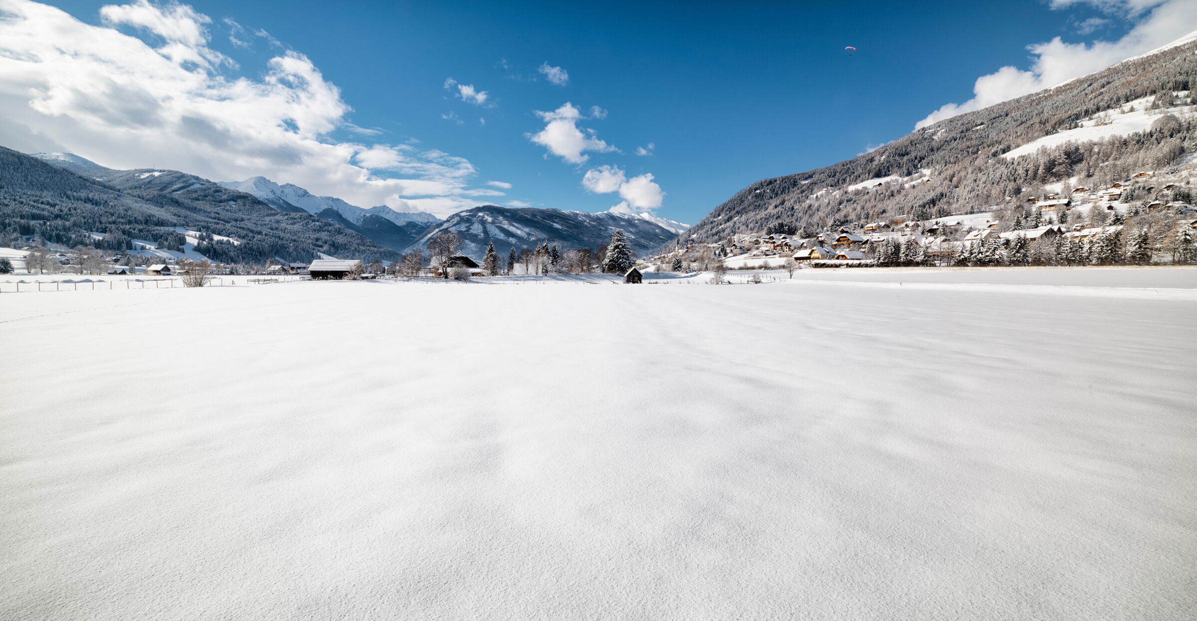 Schneebedeckte Landschaft mit Bergen und blauen Himmel im Hintergrund, idyllische Winterstimmung.