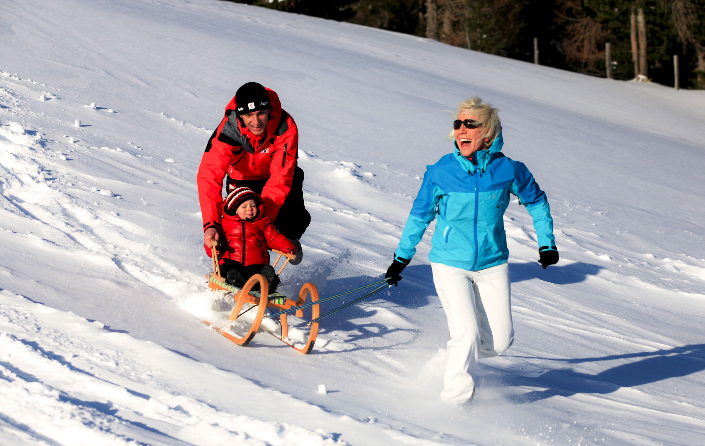 Familie beim ausgelassenen Schlittenfahren im glitzernden Schnee, strahlende Gesichter, Winterspaß.